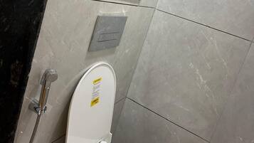 A bathroom with a white toilet, a hand dryer, and a wall-mounted flush button.