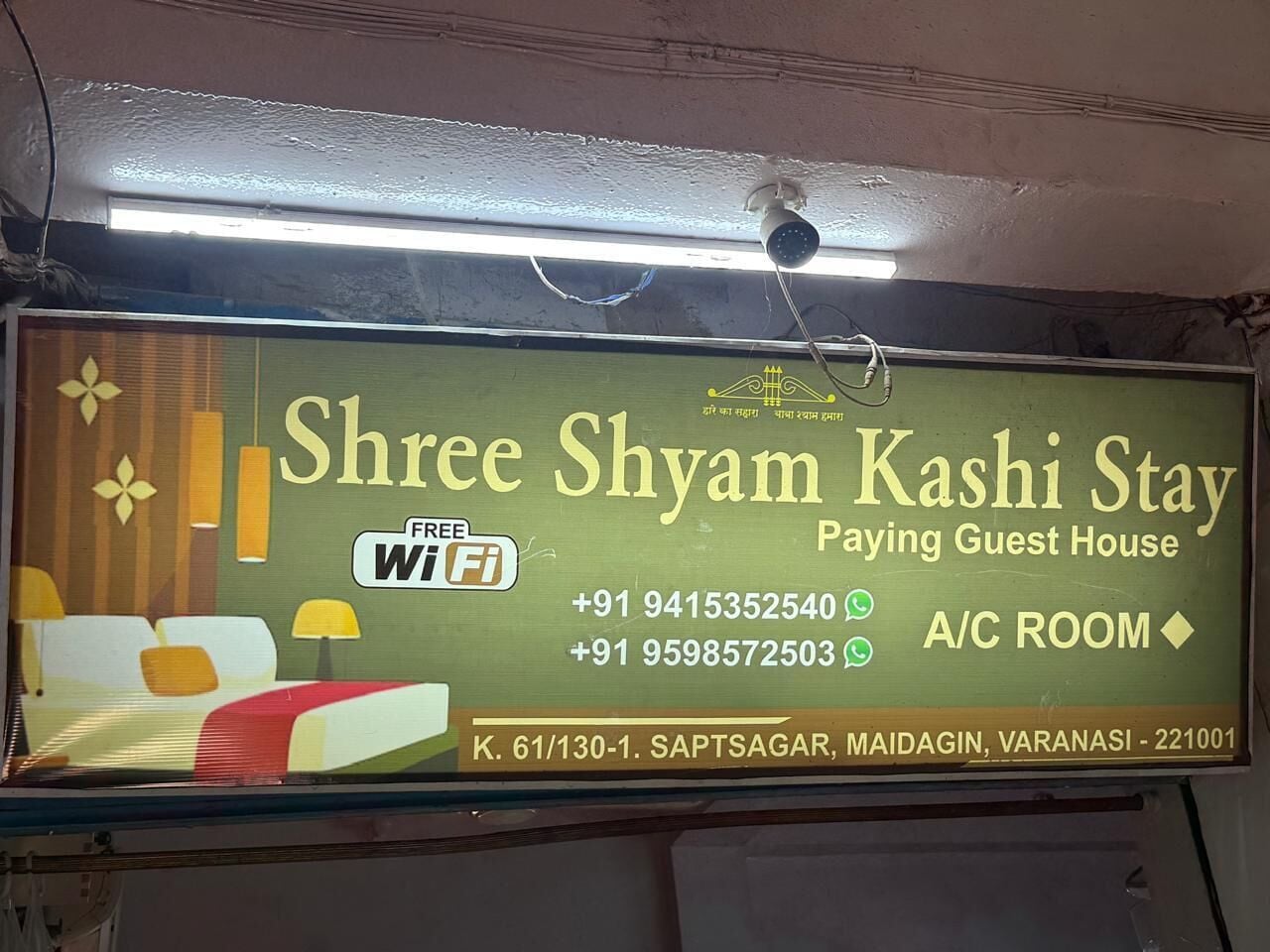 A sign for Shree Shyam Kashi Stay, a guest house with free WiFi, contact numbers, and location details.