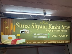 A sign for Shree Shyam Kashi Stay, a guest house with free WiFi, contact numbers, and location details. - SHRI SHYAM KASHI STAY VARANASI (Varanasi)