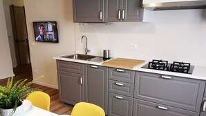 A modern kitchen with grey cabinets, a stainless steel sink, and a gas stove. There is a dining table with yellow chairs and a potted plant. - Delicious next to Florence (Scandicci)