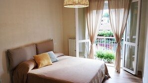 A bedroom with a large bed, a hanging light fixture, a view of the outdoors through a window with curtains, and a radiator. - Delicious next to Florence (Scandicci)
