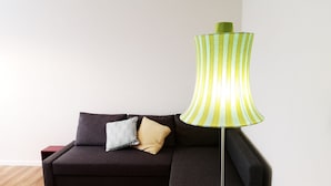 A dark-colored sofa with two patterned pillows and a green-striped floor lamp in a room with wooden flooring and white walls. - Delicious next to Florence (Scandicci)