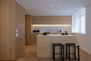 Eine moderne Küche mit Holzschnitzereien, einer zentralen Kochinsel mit Barhocker und einem großen Fenster für natürliches Licht.