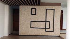A modern interior with a wooden slatted ceiling, a beige textured wall with geometric black cutouts, and a tiled floor. - Bansri Villa - Mount Lavinia  (Dehiwala-Mount Lavinia)