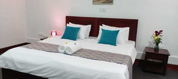Una cama bien hecha con almohadas blancas y turquesas, una toalla enrollada y una colcha estampada.