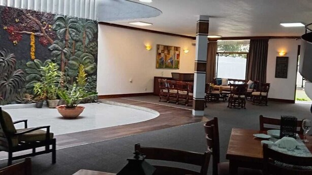A hotel lobby with a central seating area, a staircase, and a mural of tropical foliage. - Bansri Villa - Mount Lavinia  (Dehiwala-Mount Lavinia)