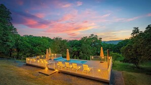 A wooden deck with a pool, lounge chairs, and umbrellas, surrounded by trees. - Alexander Valley | Hot Tub, Pool & Pickleball (Cloverdale)
