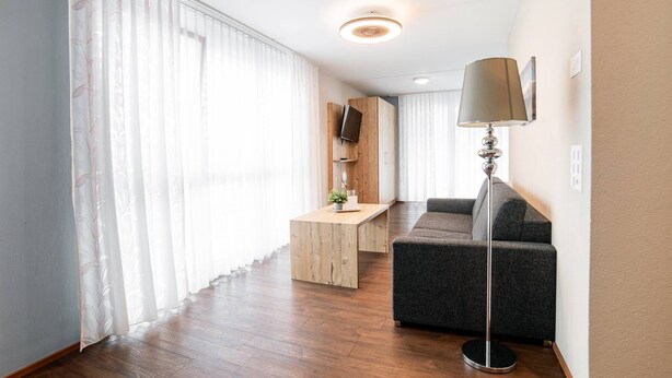 A modern living room with a wooden floor, a grey sofa, a wooden coffee table, and a floor lamp. - Wohntel - wohnen wie im Hotel (Sevelen)