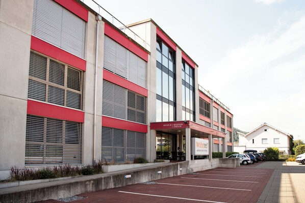 A modern building with a reception area, parking lot, and several parked cars.