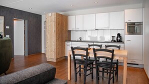 A modern kitchen with white cabinets, a wooden accent wall, and a dining area with a table and chairs. - Wohntel - wohnen wie im Hotel (Sevelen)