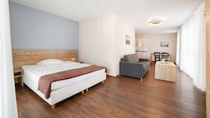 A hotel room with a wooden headboard bed, a grey sofa, a small table with chairs, and a wooden floor. - Wohntel - wohnen wie im Hotel (Sevelen)
