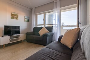 Ein modernes Wohnzimmer mit Fernseher, einer Couch, einem Sessel und einem großen Fenster mit Blick.