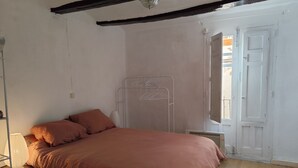 A bedroom with a bed, a bedside table, a hanging clothes rack, and a window with an open door. - Casa Julieta (Viver)