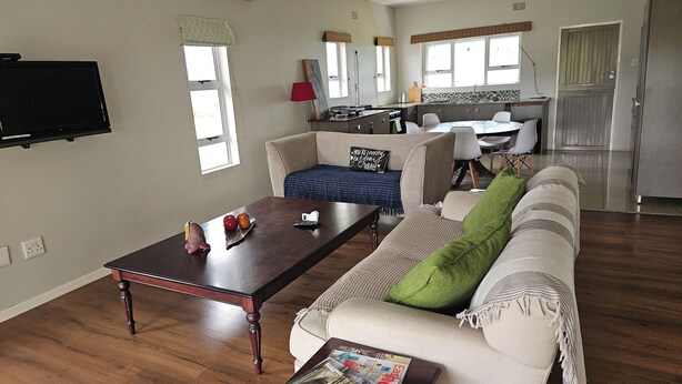 A living room with a sofa, a coffee table, and a television mounted on the wall. There is a kitchen area with a dining table and chairs visible in the background. - 5 sleeper cottage for resting and enjoying family time (Malkerns)