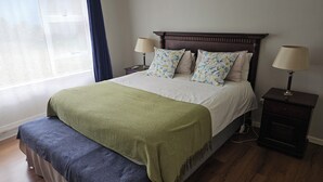 A neatly made bed with a green blanket, two matching pillows, and a wooden headboard. There are two bedside tables with lamps, and a window with curtains. - 5 sleeper cottage for resting and enjoying family time (Malkerns)