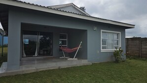 A modern house with a grey exterior, a covered porch, a hammock, and a large sliding glass door.