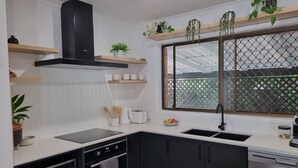 A modern kitchen with black cabinets, a black stove, a dishwasher, and a window with a view of a green fence. - Seaestaatmoffatquietbeachparklargefenced Yard (Sunshine Coast)