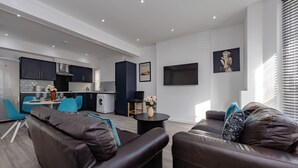 A modern living room with a sofa, a coffee table, and a TV mounted on the wall. - Apartment - Sleeps 7 - Parking - Close to Pier (Clacton-on-Sea)