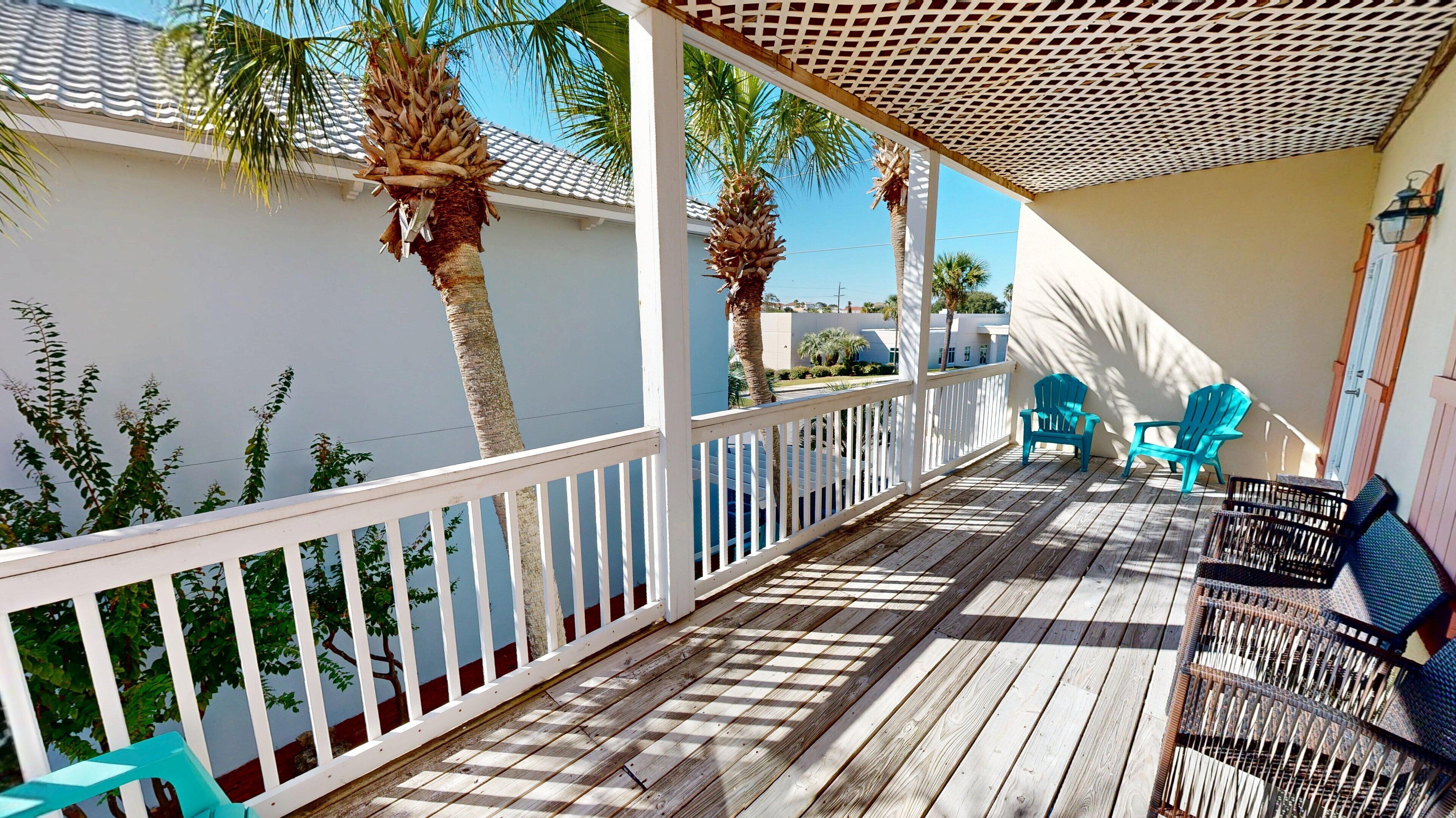 A wooden deck with a white railing, palm trees, and outdoor seating.