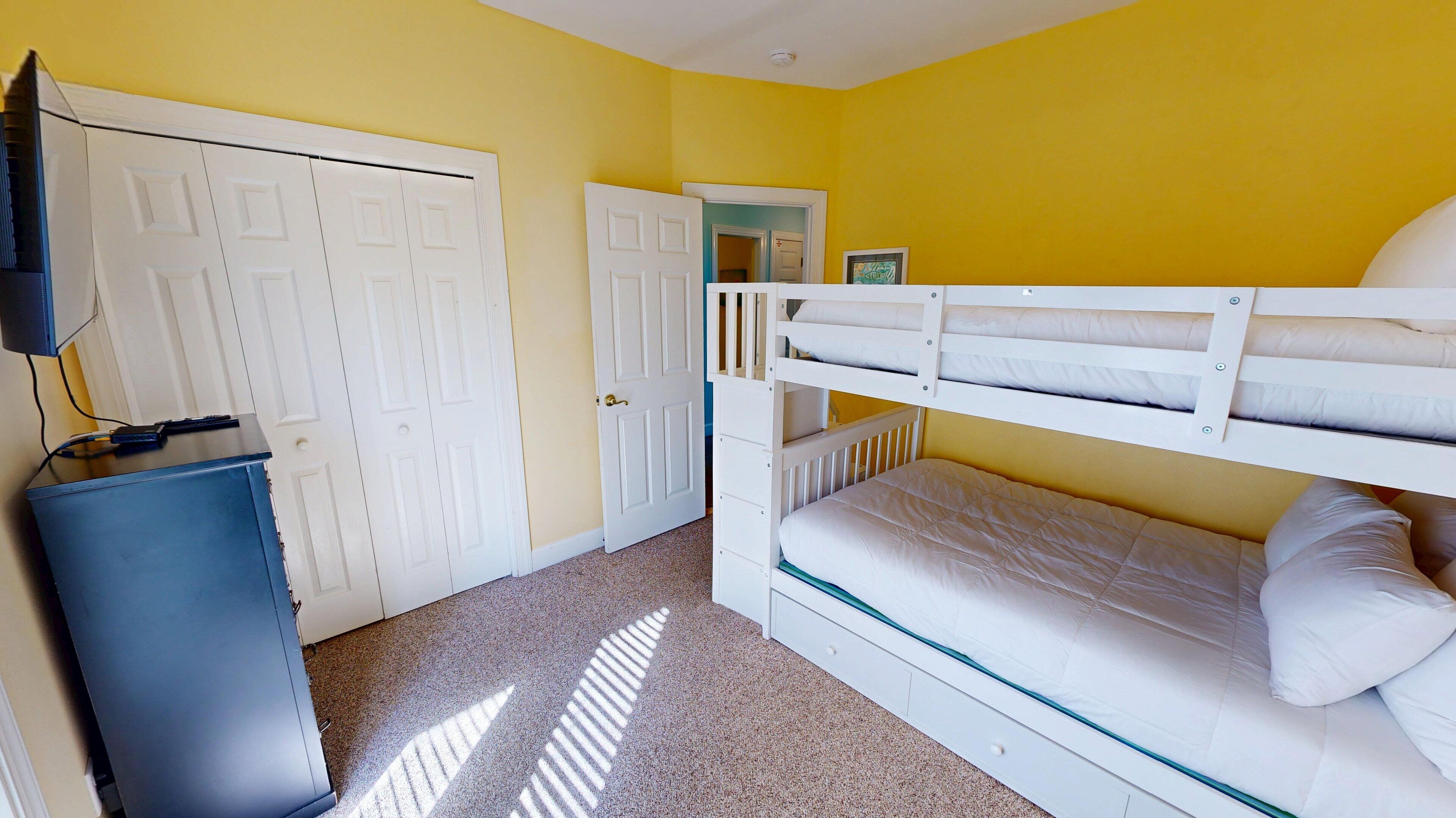 A room with bunk beds, a wardrobe, a television, and a desk.