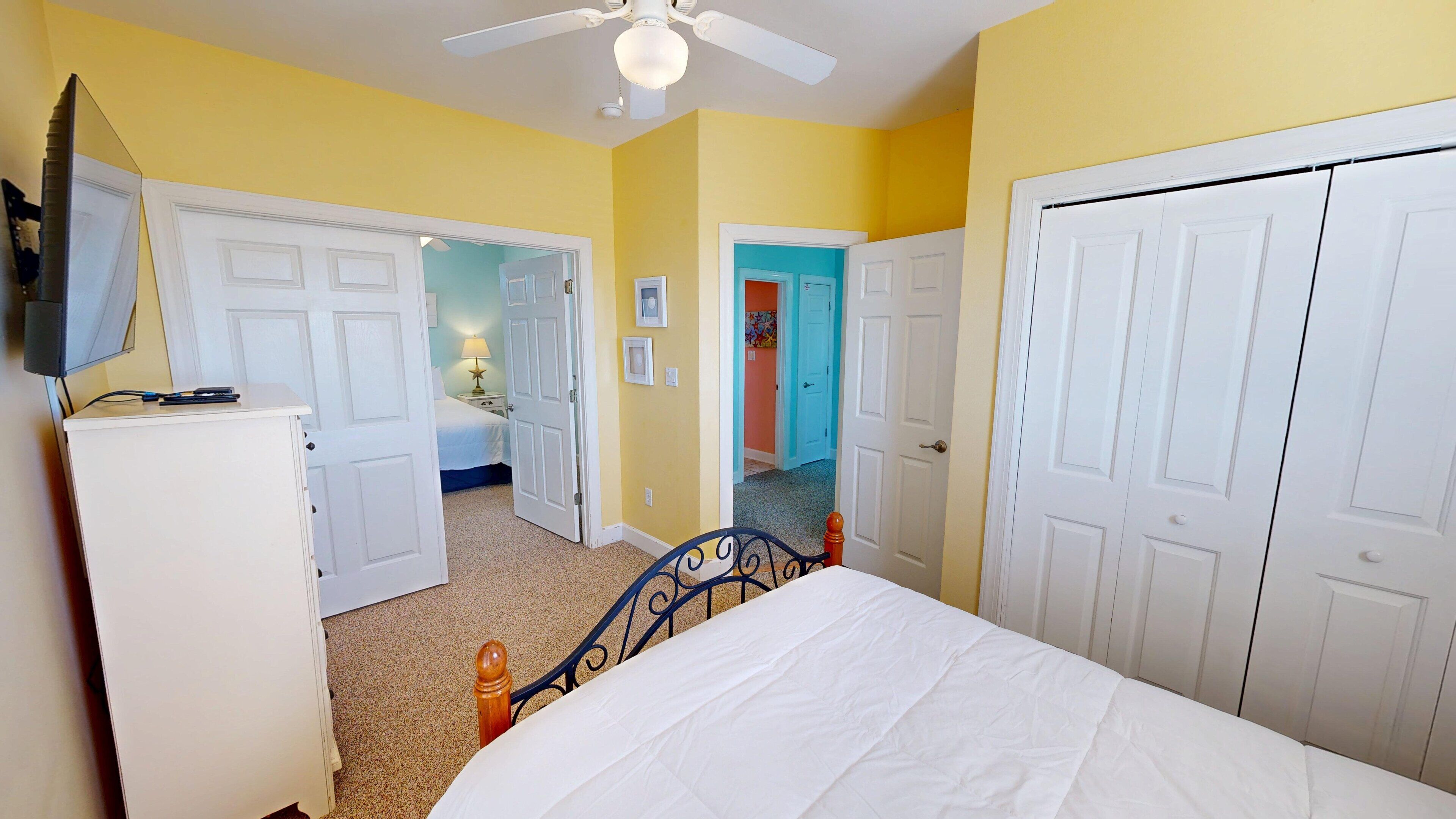 A bedroom with a bed, a dresser, a ceiling fan, and white double doors.