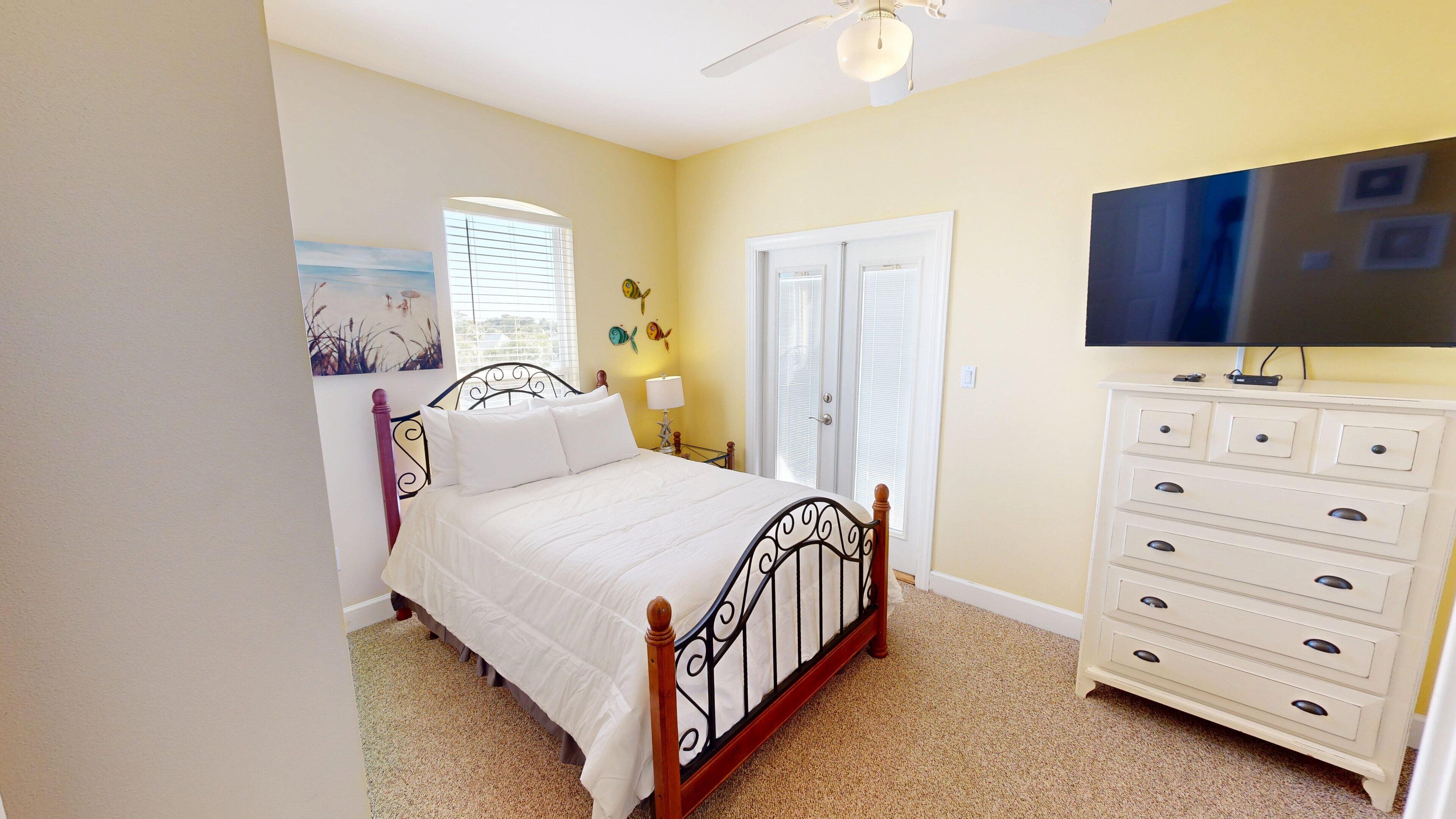A bedroom with a bed, a dresser, a television, and a door.