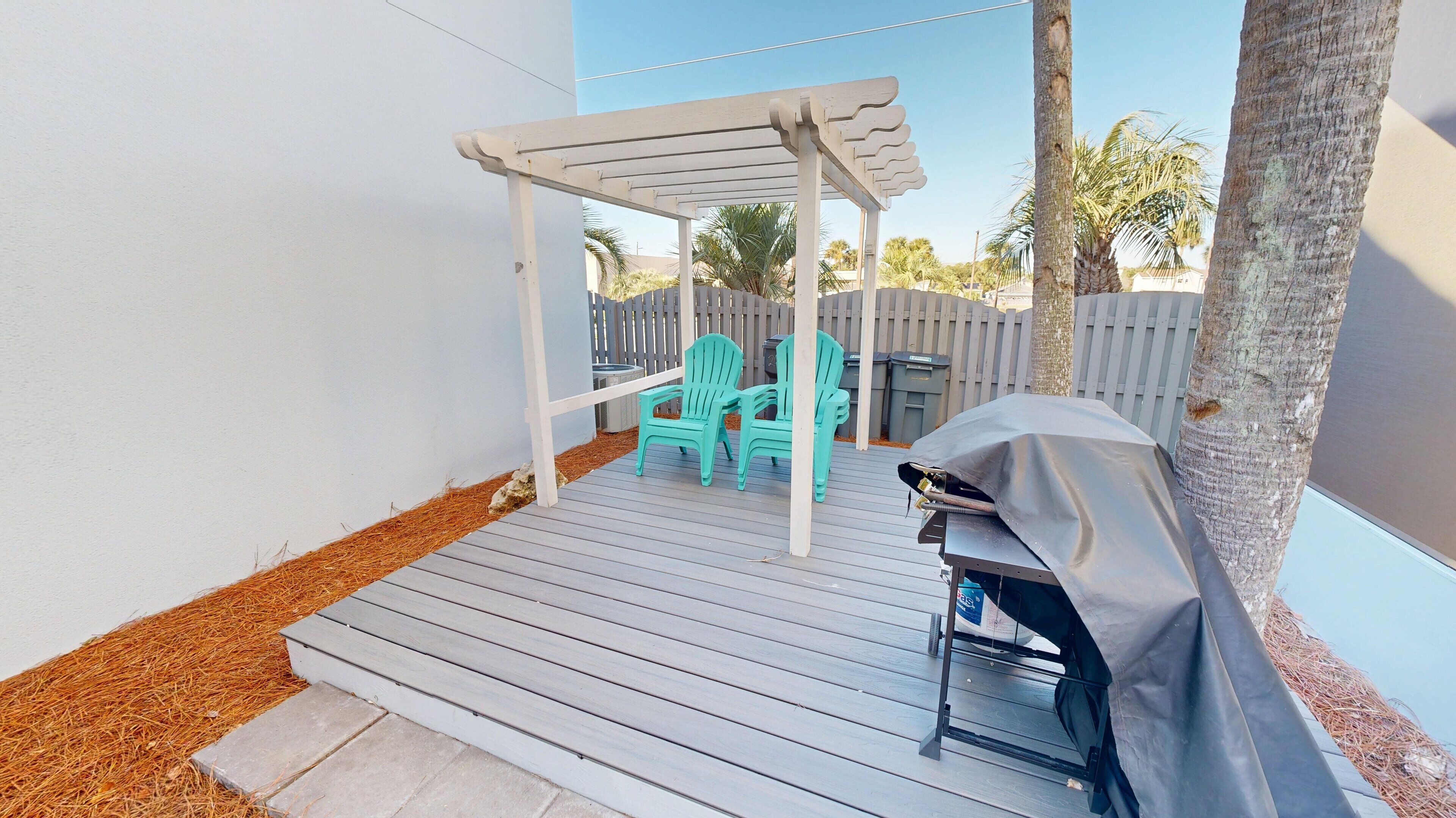 A covered patio with a grill, two turquoise chairs, and a pergola.