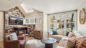 Een gezellige woonkamer met een stenen openhaard, een leren bank en een groot raam met uitzicht op de natuur.