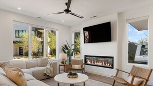 Ein modernes Wohnzimmer mit einer großen Couch, einem runden Couchtisch, einem Kamin und einem an der Wand montierten Fernseher.