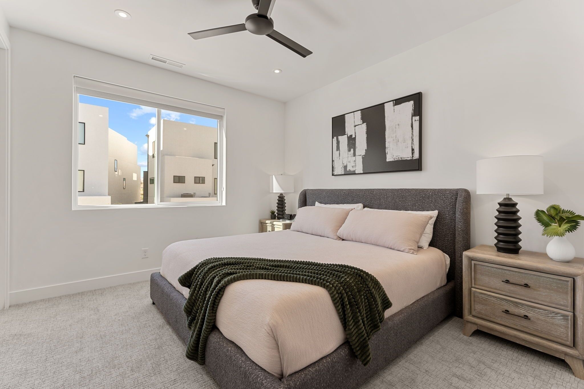 A bedroom with a bed, a nightstand, a lamp, a ceiling fan, and a window.