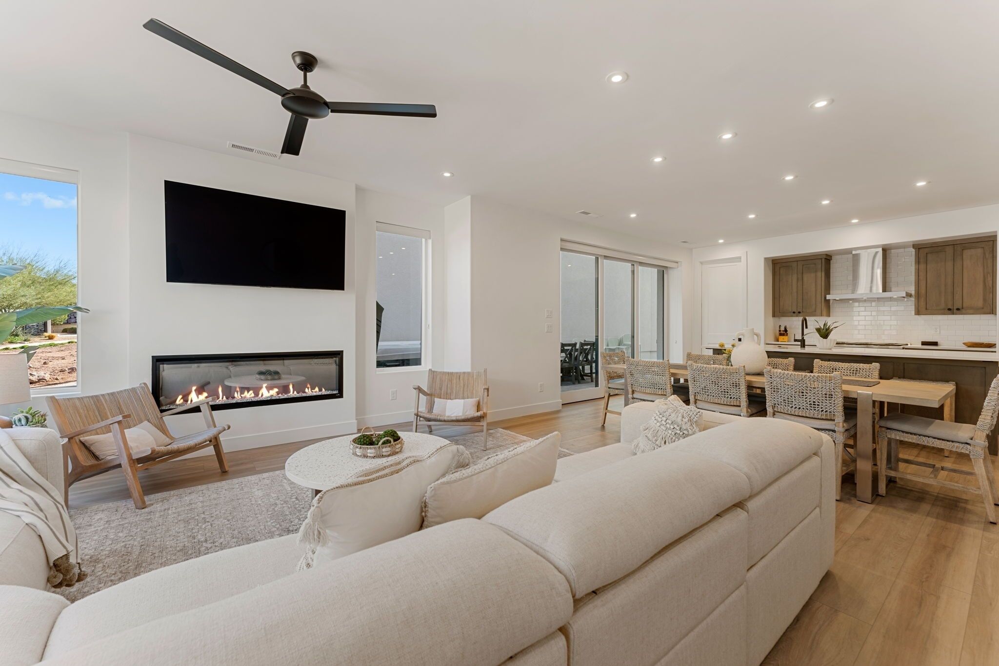 Una sala de estar moderna con chimenea, ventilador de techo y comedor con mobiliario de mimbre.