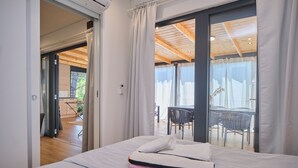 Een slaapkamer met een bed, een raam met gordijnen en uitzicht op een buiten eethoek.