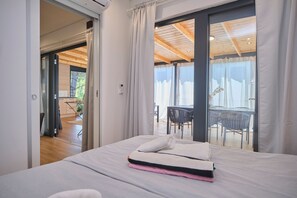 Una habitación de hotel con una cama, un puerta corrediza de vidrio que da a un área de comedor al aire libre y un techo con vigas de madera.