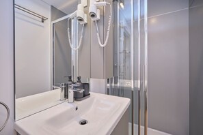 Ein modernes Badezimmer mit einem weißen Waschbecken, einem chromfarbenen Wasserhahn und einer Duschkabine aus Glas.