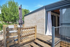 A wooden deck with a metal railing, a covered seating area, and a building entrance with a sliding door. - MH Holiday Dream - Silver Moon - Oaza Mira Campsite (Drage)