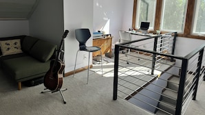 Een moderne leefruimte met een groene bank, een gitaar, een eethoek met een laptop en een trap met een metalen leuning.