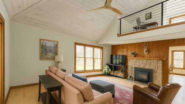 Een ruime woonkamer met een hoge plafond, een open haard, een televisie en een balkon met een leuning.