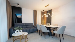 A modern living room with a dark grey sofa, a round gold-framed coffee table, and a dining area with a marble table and grey chairs. - Three-bedroom penthouse  Break with shared pool (Novalja)