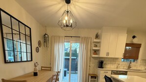 Eine moderne Küche mit Essbereich, ausgestattet mit einem Holztisch, Stühlen, einer Pendelleuchte und Blick ins Freie durch eine Glastür.