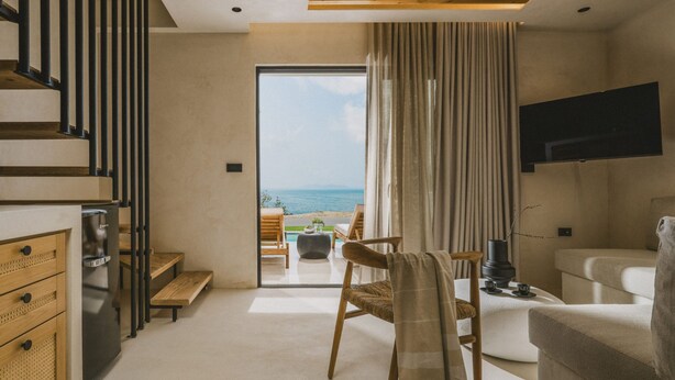 A modern living room with a view of the sea, a flat-screen TV mounted on the wall, and a staircase leading to an upper level. - Orizontas Suites 4 Syvota (Igoumenitsa)