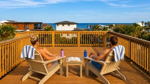 Two people sitting on deck chairs facing a wooden deck with a view of the ocean and buildings. - Oceanview Rooftop Retreat | Steps from the Beach (Jacksonville Beach)
