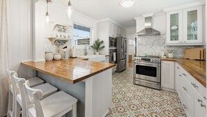 A modern kitchen with white cabinetry, a wooden island, stainless steel appliances, and patterned floor tiles. - Oceanview Rooftop Retreat | Steps from the Beach (Jacksonville Beach)