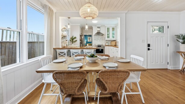 A dining area with a wooden table, white chairs, and a hanging light fixture. - Oceanview Rooftop Retreat | Steps from the Beach (Jacksonville Beach)
