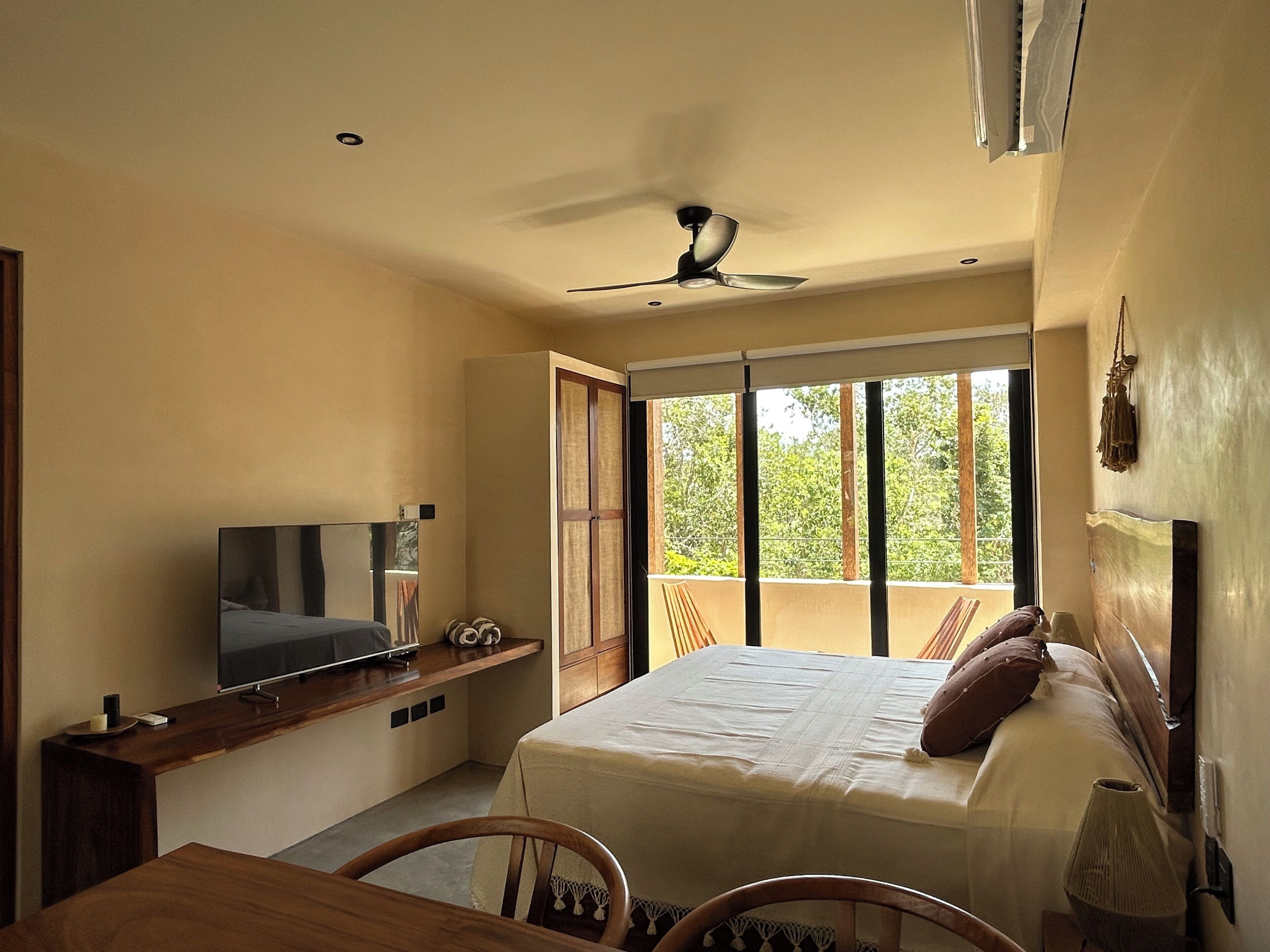 Een slaapkamer met een bed, een televisie, een balkon en een plafondventilator.