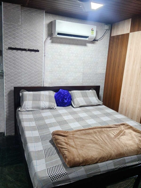 A bed with a patterned bedspread, two pillows, a blue decorative item, and a brown blanket. - Nirmal Cottage (Gobichettipalayam)