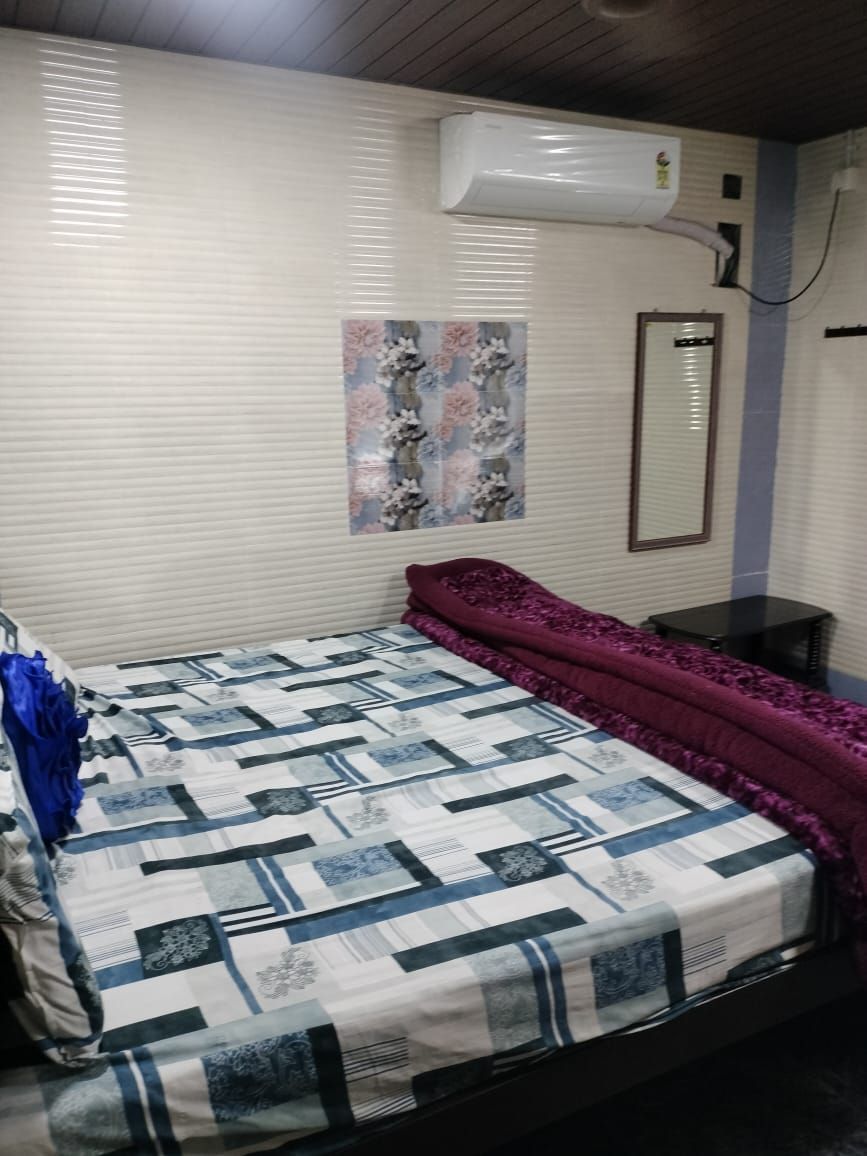 A bedroom with a bed, a wall-mounted air conditioner, a mirror, and a floral artwork on the wall.