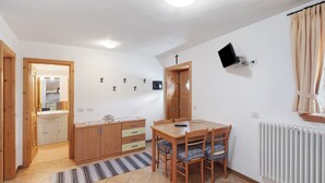 Une pièce comprenant une table à manger, des chaises, un coin cuisine et un radiateur.