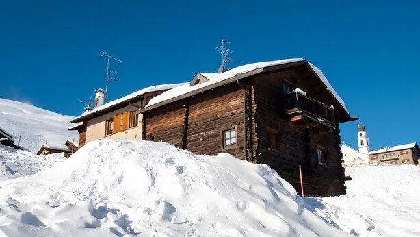 Une cabane en bois avec un toit en pente, entourée de neige, et une église avec un clocher en arrière-plan.
