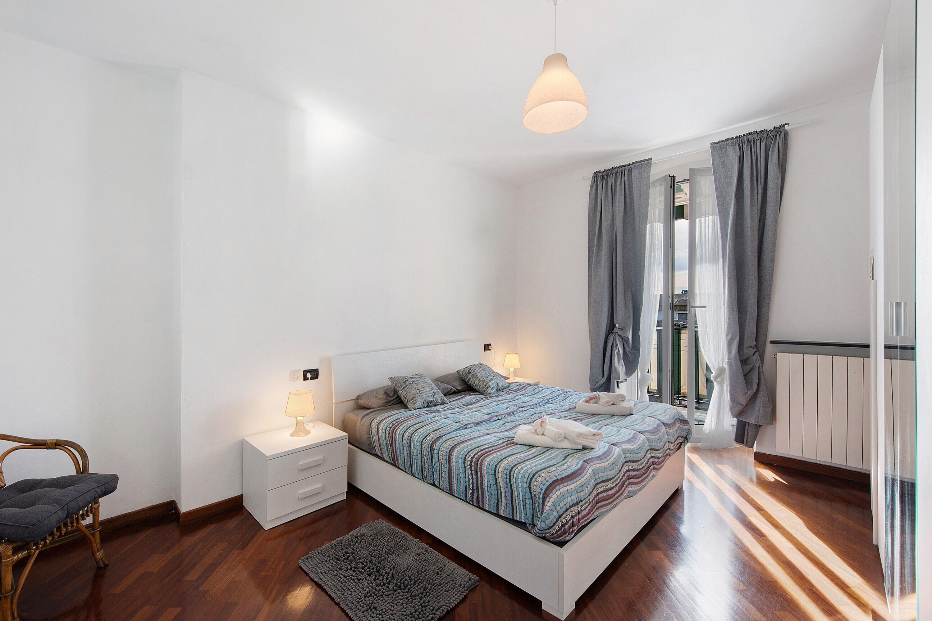 A bedroom with a bed, bedside tables, a chair, and a hanging light fixture.