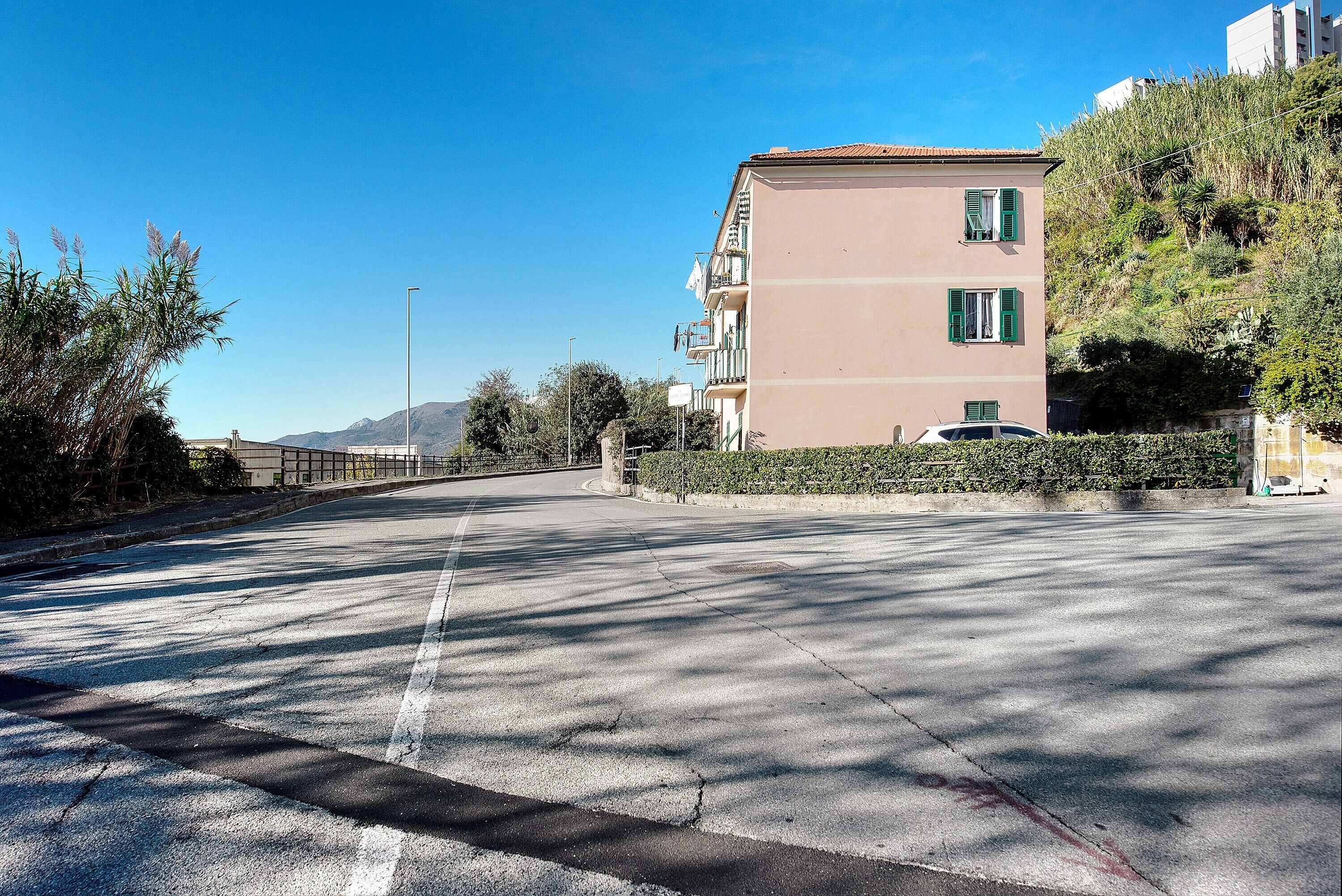 Eine freie Straße mit einem Gebäude auf der rechten Seite, einem davor parkenden Auto und einem wolkenlosen Himmel.